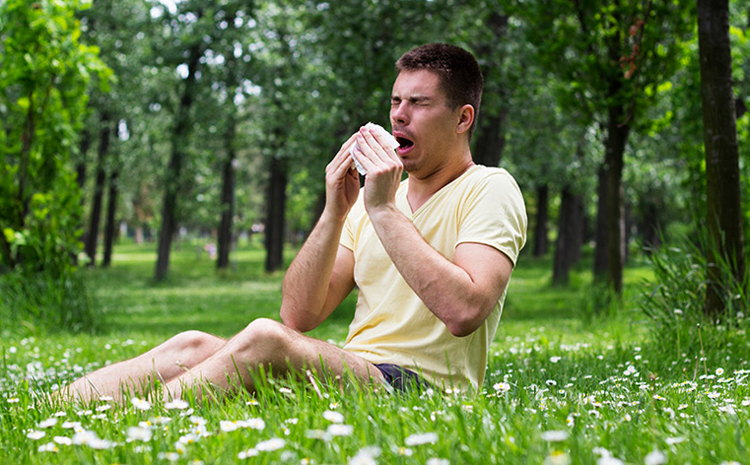 Мужчина на траве чихает